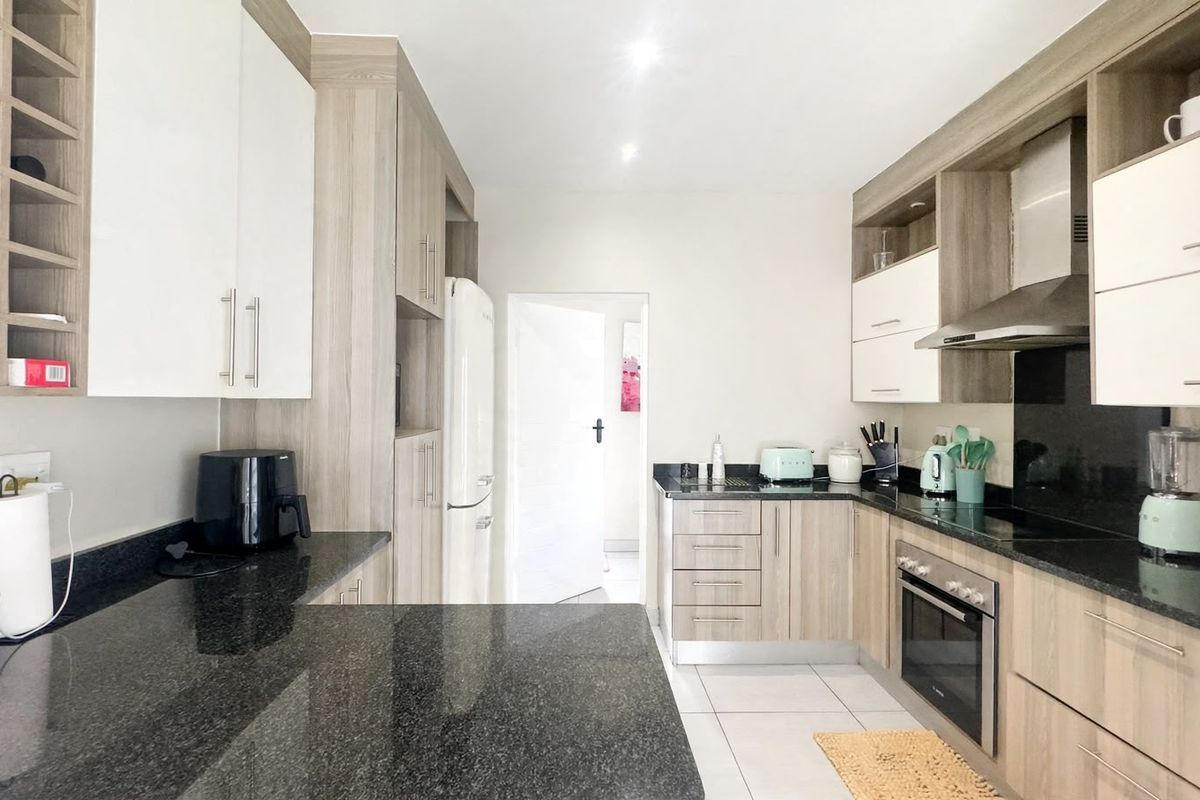 Modern kitchen featuring light wood-grain cabinetry, contrasting black granite countertops, stainless steel appliances, and tiled flooring.