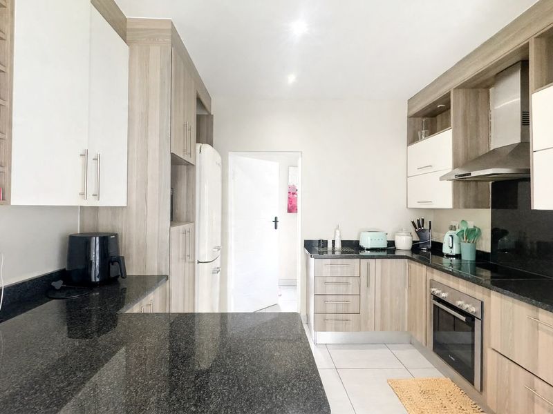 Modern kitchen featuring light wood-grain cabinetry, contrasting black granite countertops, stainless steel appliances, and tiled flooring.