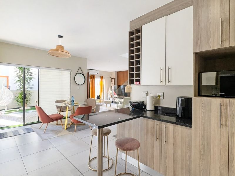 Modern open-plan living area featuring a contemporary kitchen with granite countertops, breakfast bar, and seamless flow to the outdoor patio through sliding glass doors.
