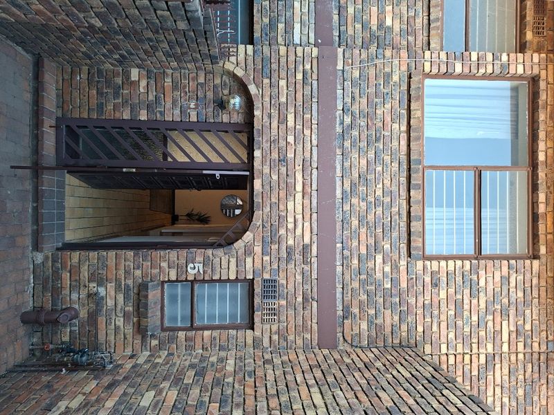 Front entrance of the apartment featuring a face brick facade, secure metal gate, and window security bars.
