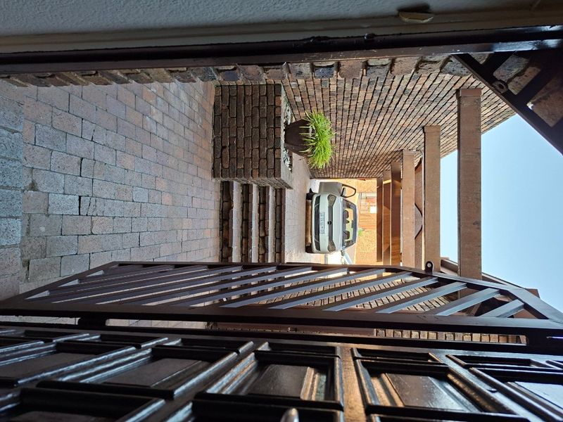 A view of the property entrance featuring brick paving, a timber pergola structure, and a secure metal gate.