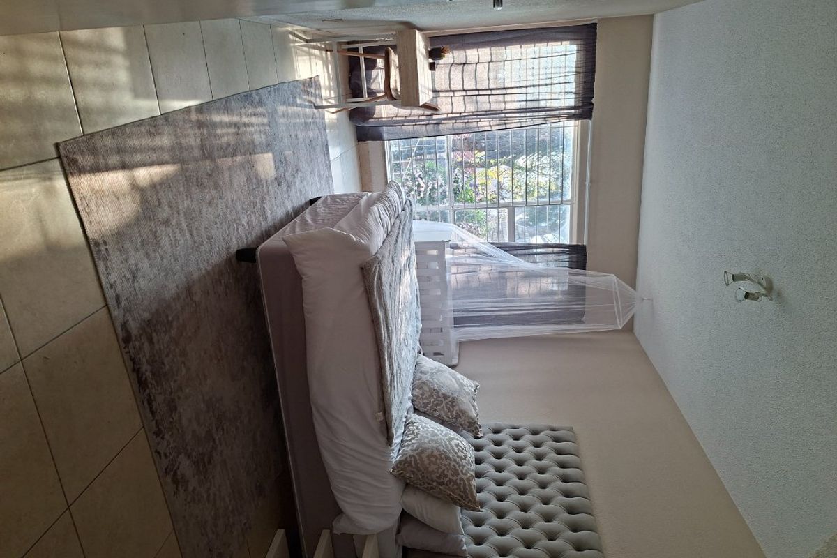 A bedroom featuring tiled flooring, a large window with security bars, and a ceiling light fixture.