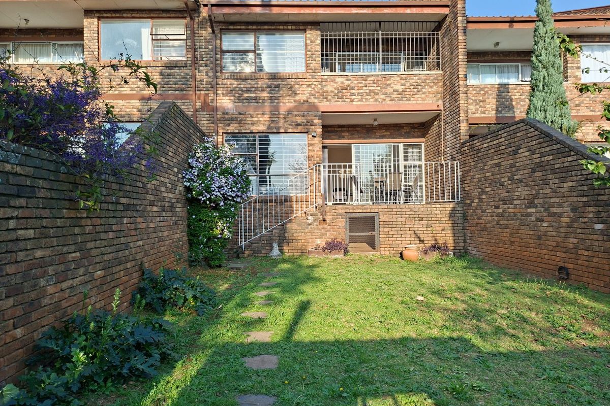 Rear view of the apartment featuring a private garden, brick facade, and a raised patio area with security railings.