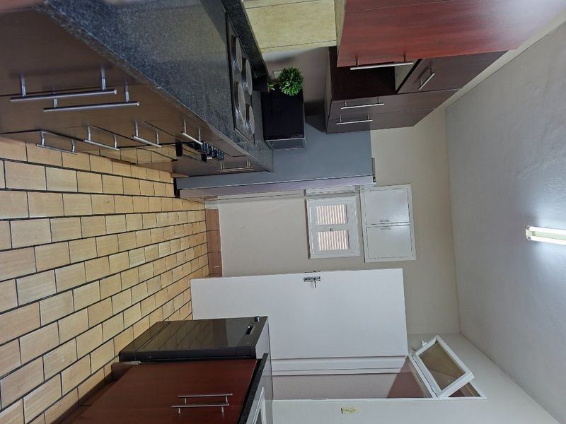 A functional kitchen featuring dark wood cabinetry, granite countertops, a built-in hob, and tiled flooring.