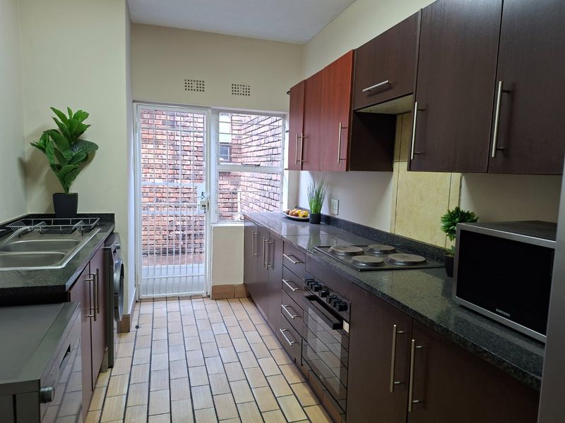 A functional kitchen featuring dark wood cabinetry, granite countertops, built-in oven and hob, and direct access to an exterior area via a security gate.