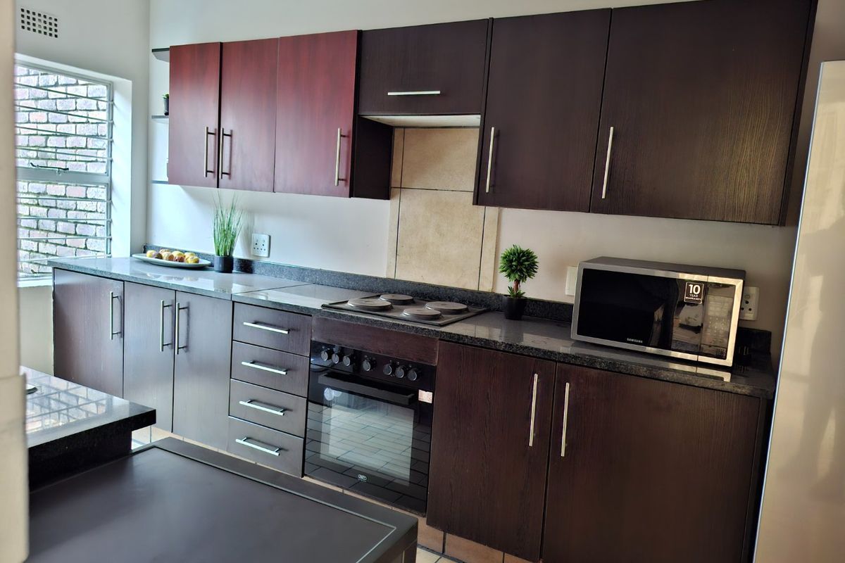 A functional kitchen featuring dark wood cabinetry, granite countertops, an integrated electric hob, oven, and extractor fan with tiled flooring.