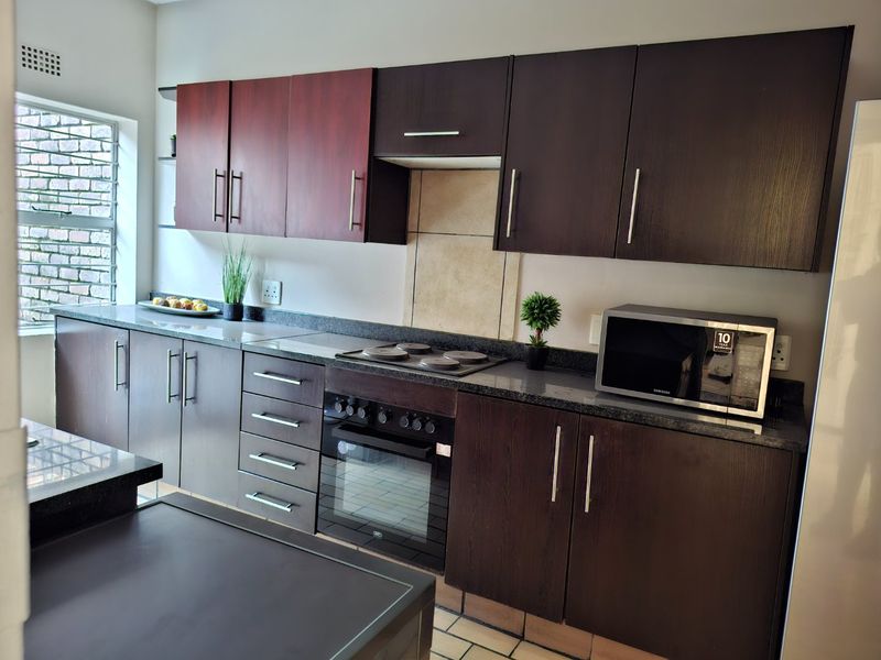 A functional kitchen featuring dark wood cabinetry, granite countertops, an integrated electric hob, oven, and extractor fan with tiled flooring.