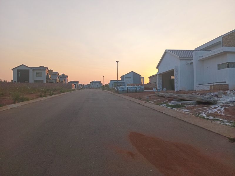 A view of a residential street in a developing estate at sunset, featuring paved roads and surrounding modern residential construction.