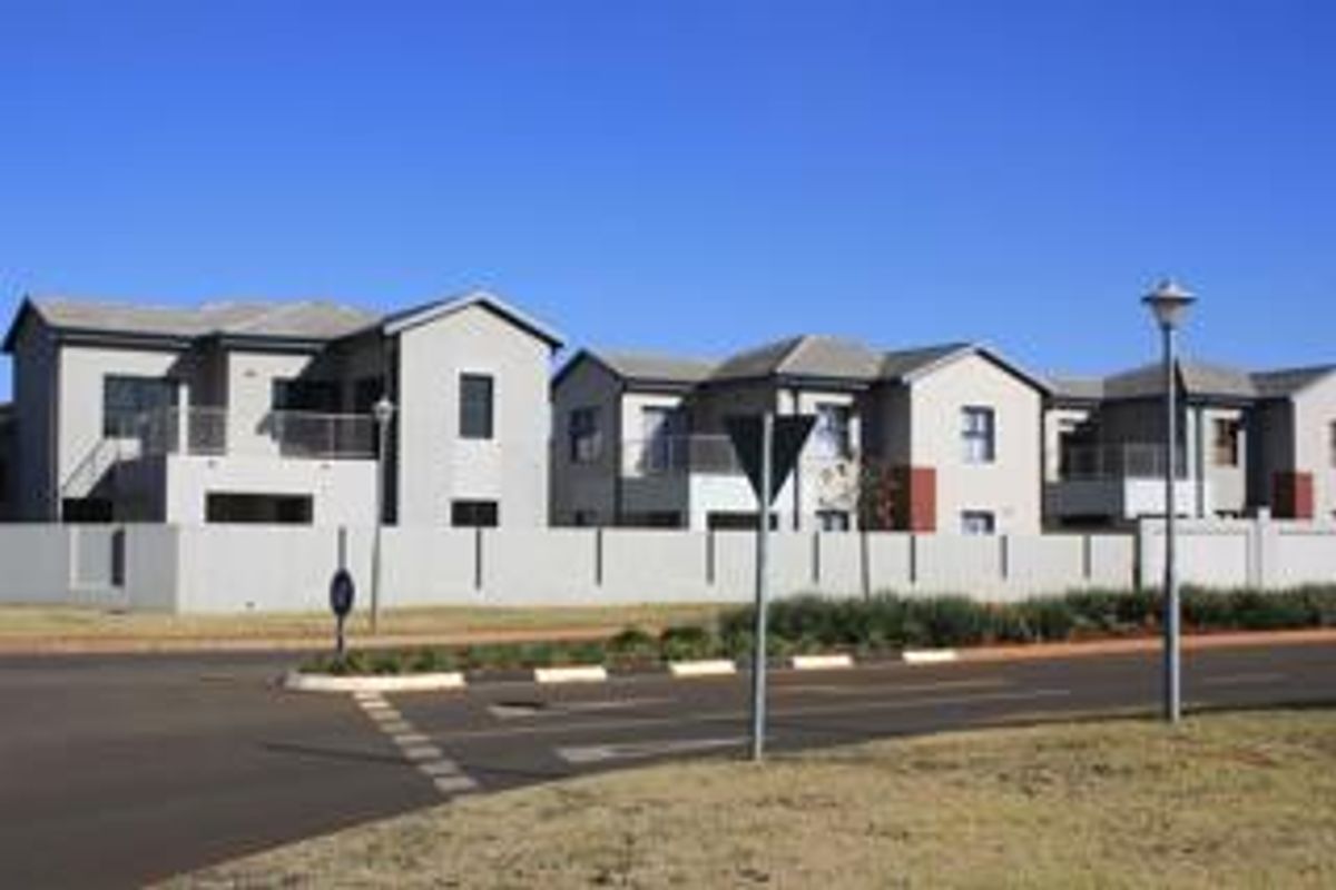 A street-level view of a modern residential complex featuring multi-story units with perimeter walling and paved road access.