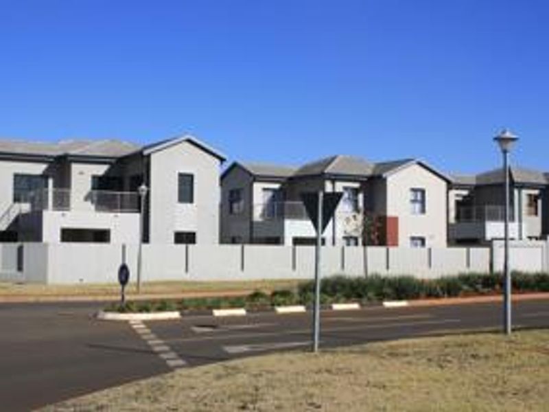 A street-level view of a modern residential complex featuring multi-story units with perimeter walling and paved road access.