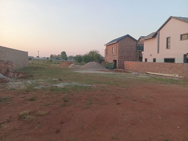 A view of a vacant residential plot featuring boundary walls and adjacent construction, offering a blank canvas for development.