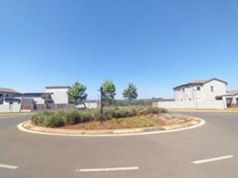 A view of a residential street roundabout featuring landscaped greenery and surrounding modern residential properties.