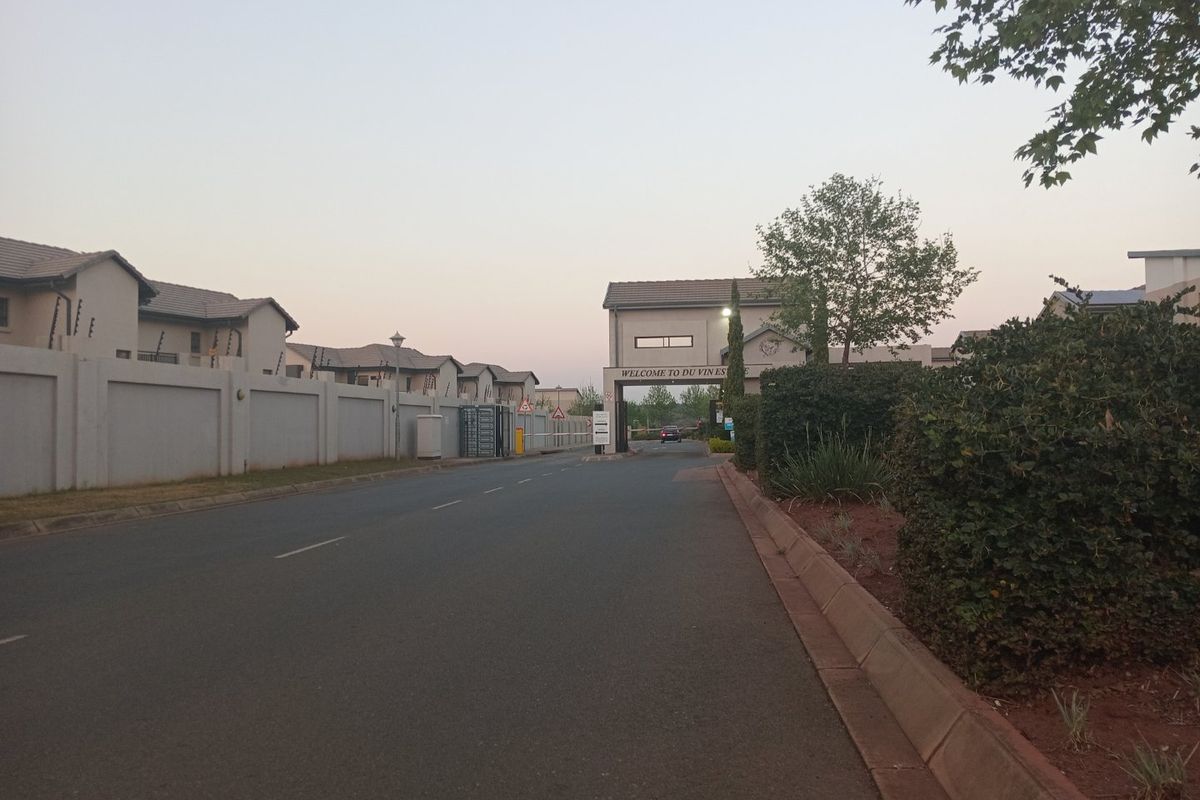 View of the secure entrance gatehouse and perimeter walling for the residential estate, featuring paved road access and established landscaping.