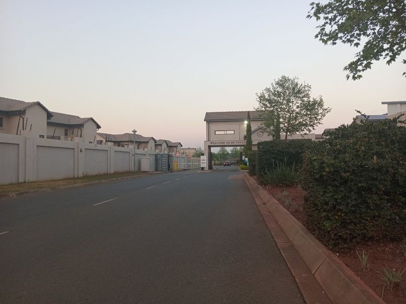 View of the secure entrance gatehouse and perimeter walling for the residential estate, featuring paved road access and established landscaping.
