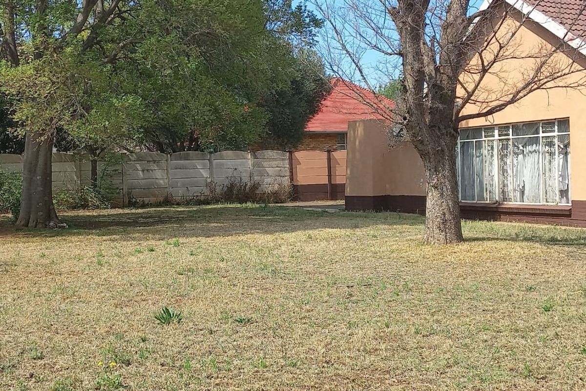 A view of the rear garden and house exterior, featuring a large lawn, mature trees, and a precast concrete boundary wall.