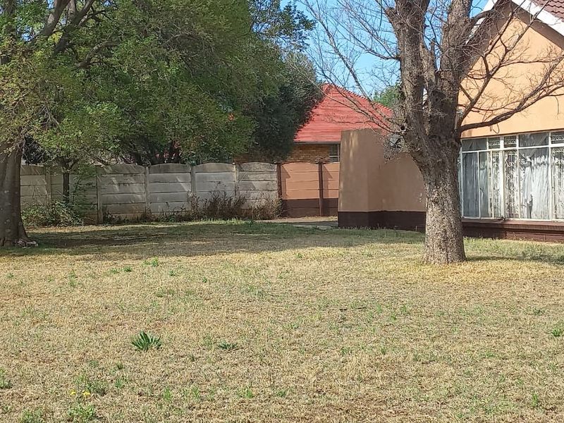 A view of the rear garden and house exterior, featuring a large lawn, mature trees, and a precast concrete boundary wall.