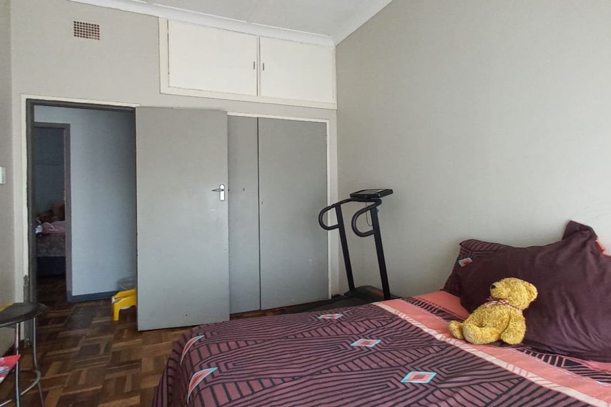 A bedroom featuring parquet flooring and built-in cupboards, offering a functional space with potential for cosmetic updates.