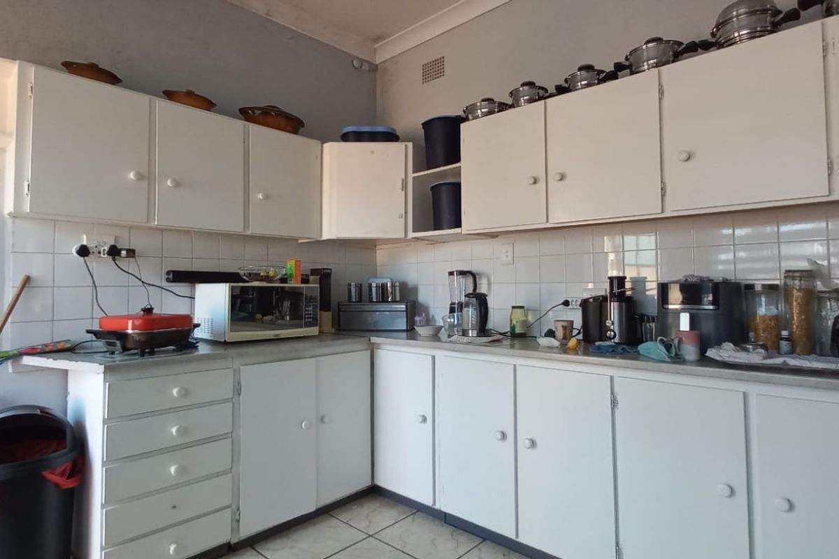 A functional kitchen featuring white built-in cabinetry, tiled backsplash, and tiled flooring, offering a practical layout with potential for cosmetic updates.