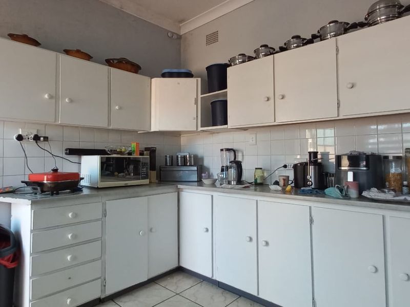 A functional kitchen featuring white built-in cabinetry, tiled backsplash, and tiled flooring, offering a practical layout with potential for cosmetic updates.