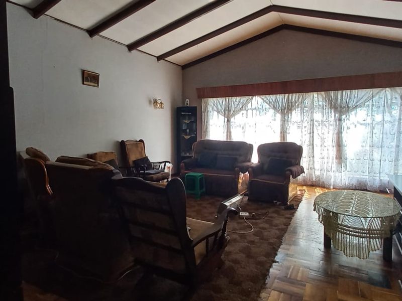Spacious living room featuring exposed timber ceiling beams, parquet flooring, and a stone feature wall, offering a classic layout with ample natural light.