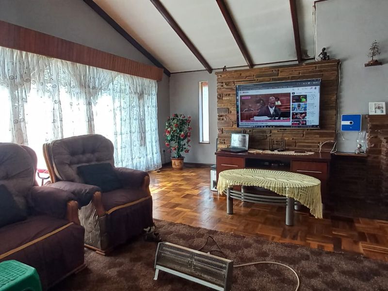 Spacious living room featuring a vaulted ceiling with exposed timber beams, a stone feature wall with a fireplace, and classic parquet flooring.
