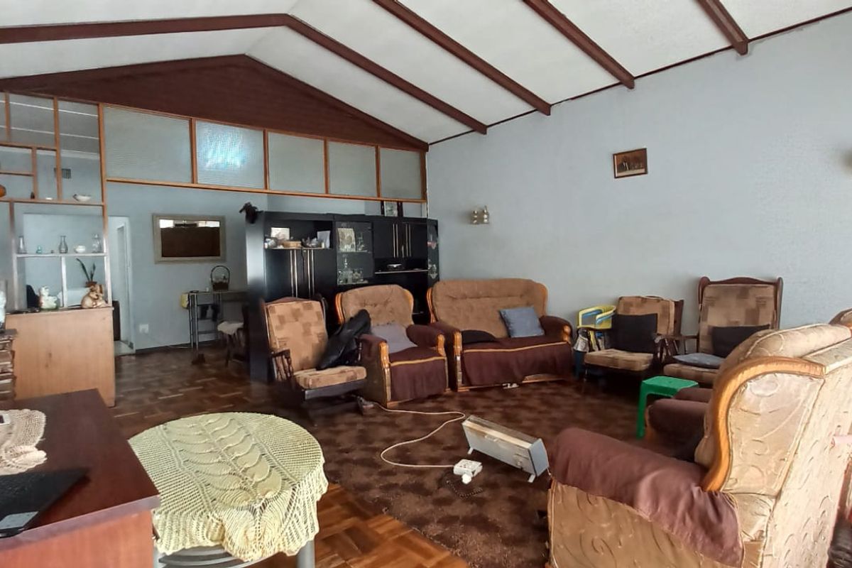 Spacious living room featuring exposed timber ceiling beams, parquet flooring, and a stone feature wall, offering a traditional layout with potential for modernization.
