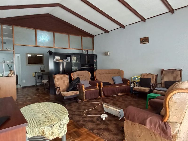 Spacious living room featuring exposed timber ceiling beams, parquet flooring, and a stone feature wall, offering a traditional layout with potential for modernization.