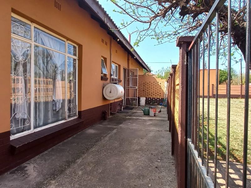 Rear exterior view of the property featuring a concrete walkway, boundary wall, and external geyser unit.