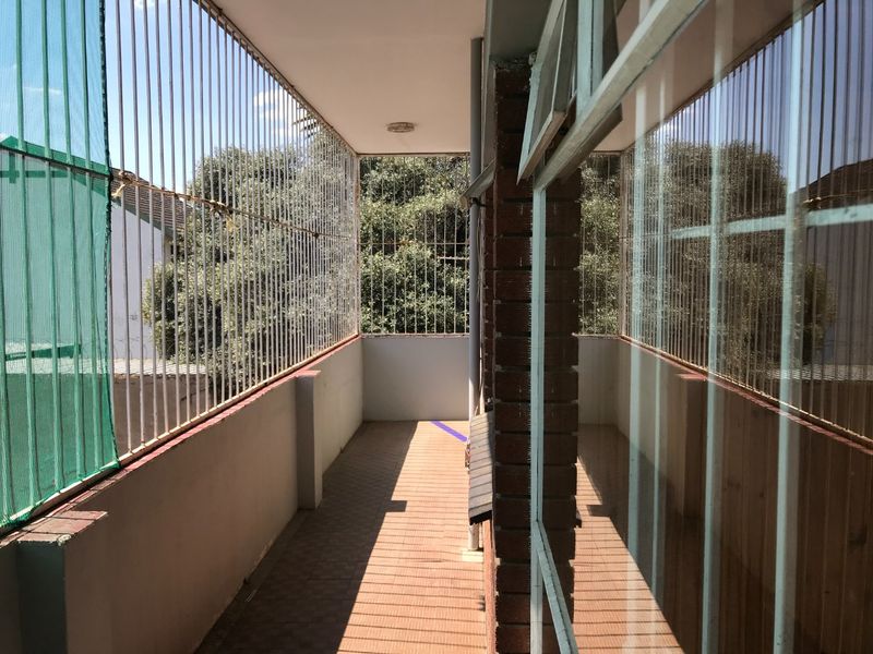 A narrow, enclosed balcony featuring security bars, tiled flooring, and a brick pillar, offering a functional outdoor space with potential for modernization.