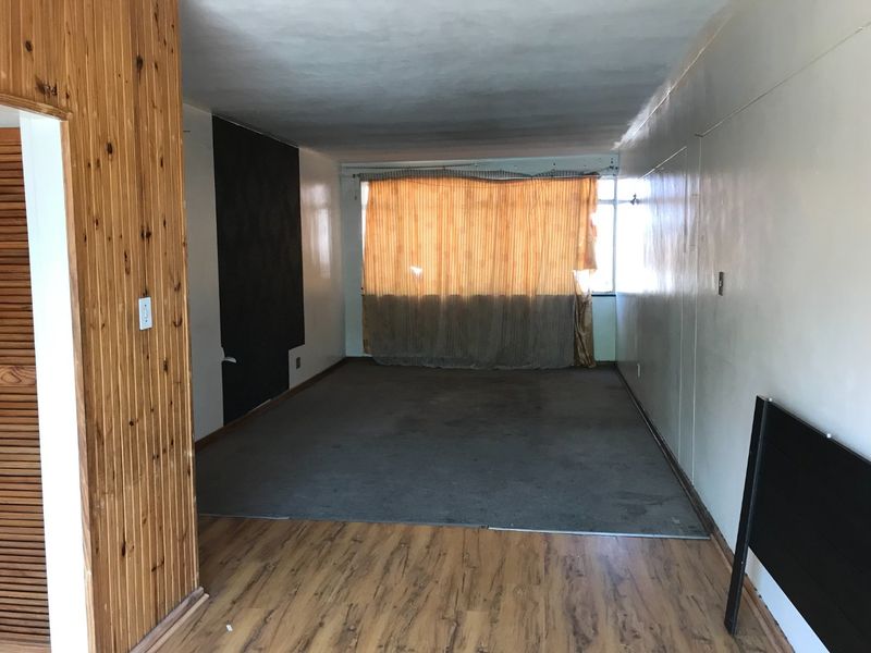 An empty living room featuring a mix of timber wall paneling, laminate flooring, and worn carpeting, requiring cosmetic updates to improve its overall appeal.