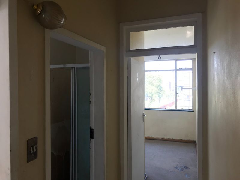 A view through a hallway leading into an adjacent room, featuring dated wall finishes and basic architectural fixtures in need of refurbishment.