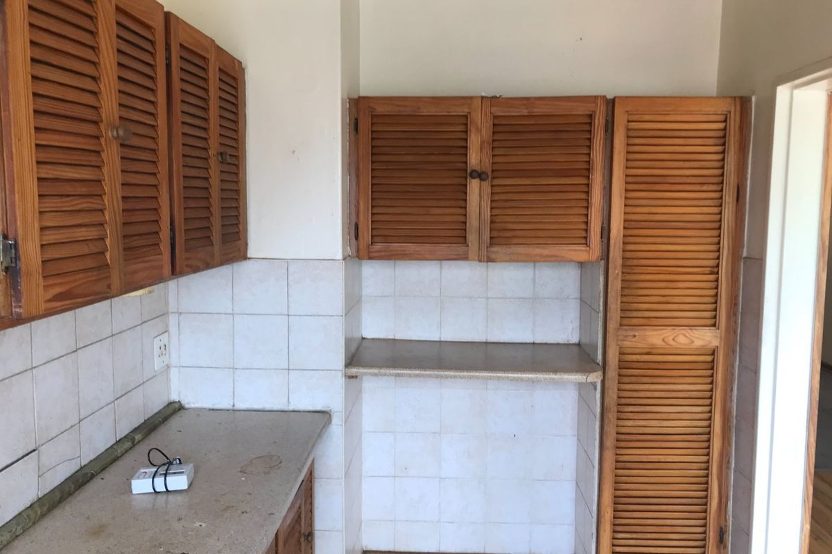 A dated kitchen area featuring louvered wooden cabinetry, tiled backsplash, and laminate countertops, offering potential for a modern renovation.