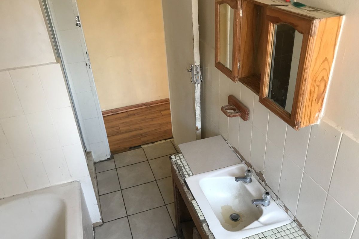 A dated bathroom featuring a built-in vanity, wall-mounted medicine cabinet, and bathtub, requiring renovation to update the finishes and fixtures.