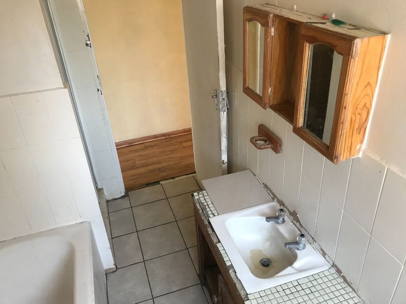 A dated bathroom featuring a built-in vanity, wall-mounted medicine cabinet, and bathtub, requiring renovation to update the finishes and fixtures.