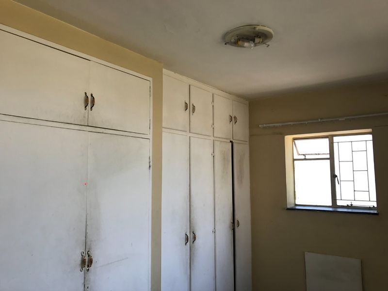 A bedroom featuring extensive built-in cupboards and a window with security bars, requiring cosmetic updates to the cabinetry and finishes.
