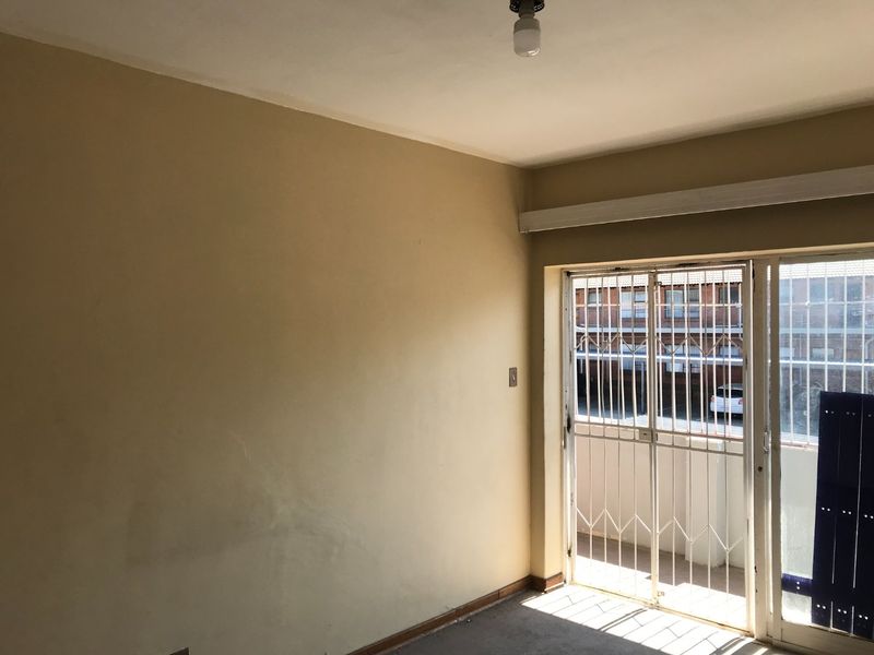 An empty living area featuring a sliding door with a security gate, providing access to an outdoor space.