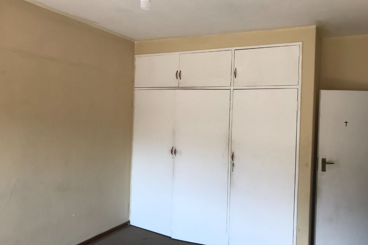 An empty bedroom featuring built-in cupboards with overhead storage, requiring cosmetic updates to the walls and flooring.