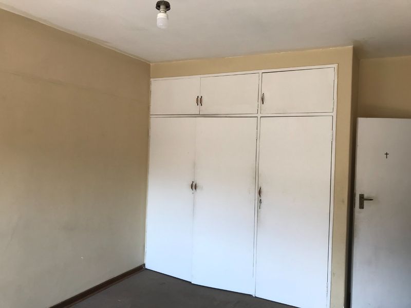 An empty bedroom featuring built-in cupboards with overhead storage, requiring cosmetic updates to the walls and flooring.
