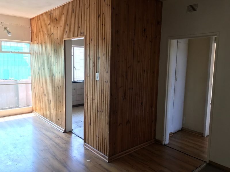 An empty living area featuring dated timber wall paneling and laminate flooring, with access to adjacent rooms and a balcony.