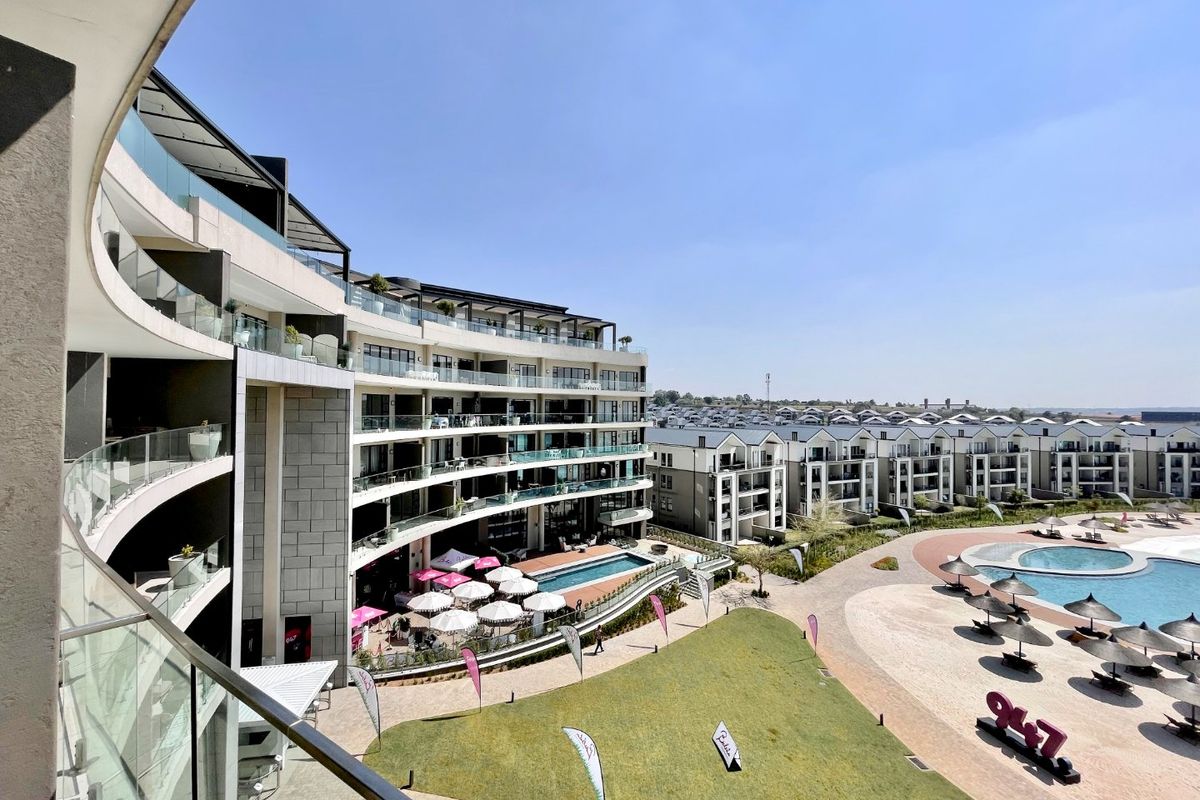 Elevated view overlooking a modern apartment complex, featuring a swimming pool, landscaped grounds, and contemporary architectural design with glass balcony balustrades.