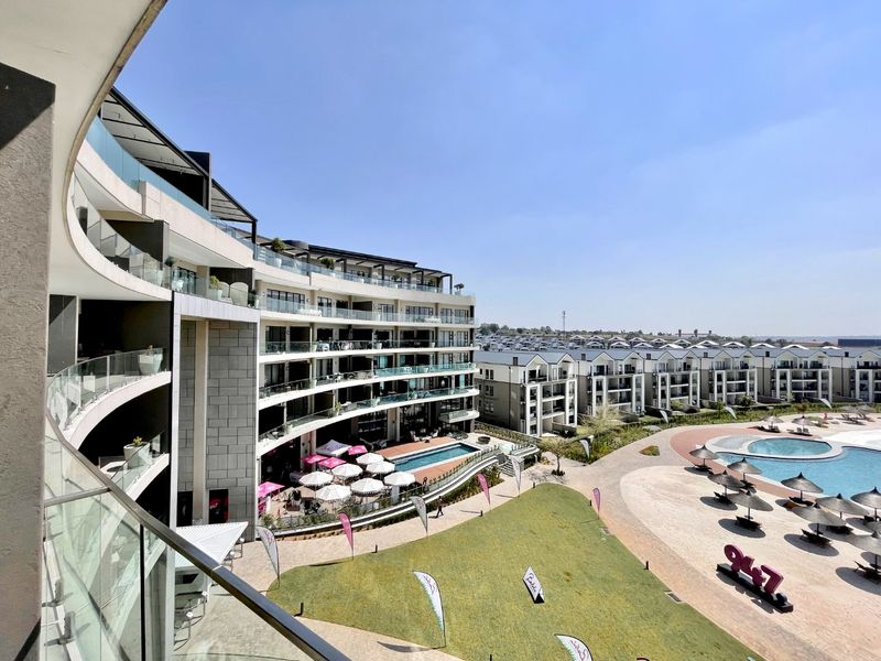 Elevated view overlooking a modern apartment complex, featuring a swimming pool, landscaped grounds, and contemporary architectural design with glass balcony balustrades.