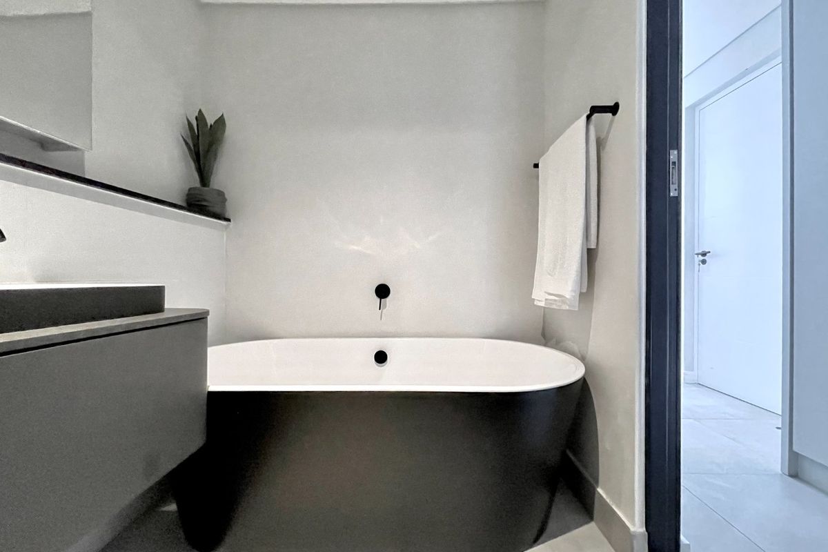Modern bathroom featuring a sleek black freestanding bathtub, wall-mounted faucet, and minimalist vanity cabinet with clean contemporary finishes.
