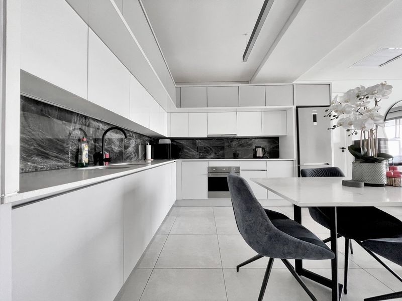 Modern open-plan kitchen featuring sleek white cabinetry, dark marble-effect splashbacks, integrated appliances, and high-quality tiled flooring.