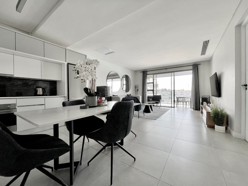 Modern open-plan living area featuring a sleek kitchen with built-in cabinetry, stone countertops, and seamless flow to a balcony through large sliding glass doors.