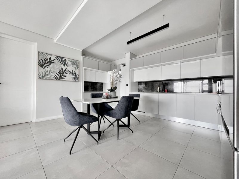 Modern open-plan kitchen and dining area featuring sleek white cabinetry, dark stone splashbacks, large format floor tiles, and contemporary recessed ceiling lighting.
