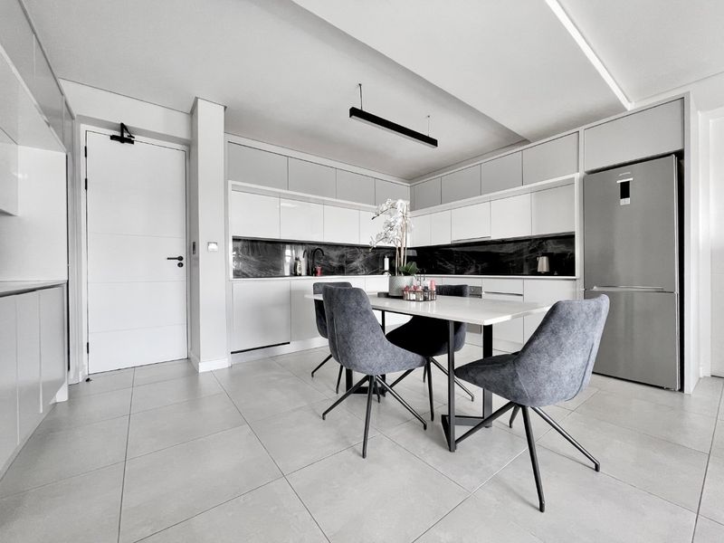 Modern open-plan kitchen and dining area featuring sleek cabinetry, stone splashbacks, and large format floor tiles in a contemporary neutral palette.