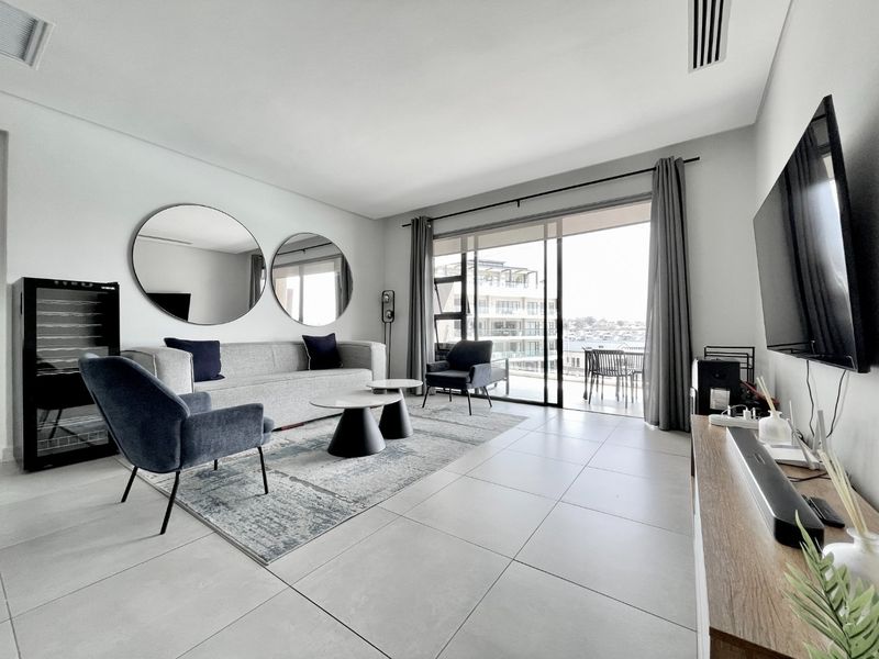 Modern living room featuring large format floor tiles, ducted air conditioning, and seamless access to a private balcony with outdoor views.