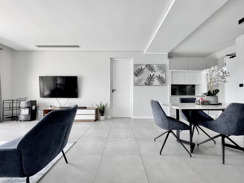 Modern open-plan living and dining area featuring neutral tiled flooring, recessed ceiling lighting, and integrated cabinetry in a clean, contemporary aesthetic.