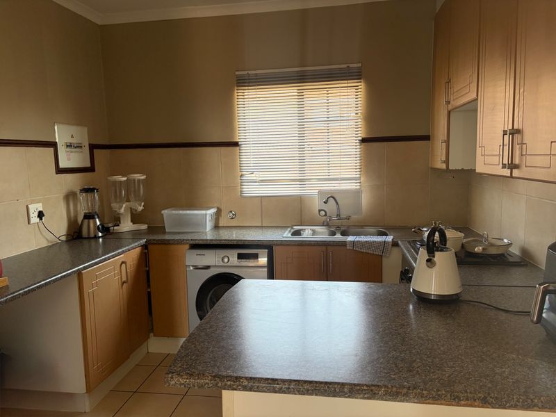 Functional kitchen featuring laminate cabinetry, ample countertop space, a double bowl sink, and a built-in hob with tiled splashback.