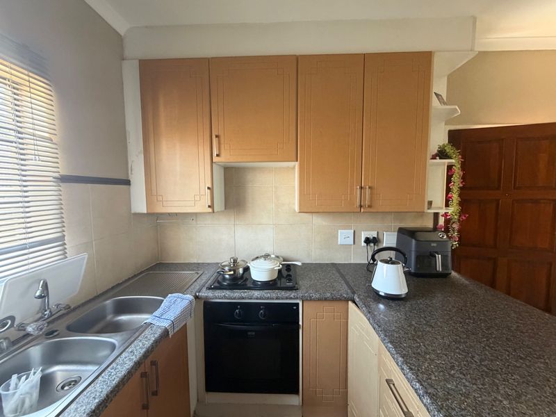 Compact kitchen featuring wooden cabinetry, a built-in oven with hob, double sink, and granite-look countertops with a tiled backsplash.